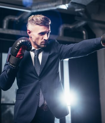 handsome businessman in suit boxing with punching bag in gym